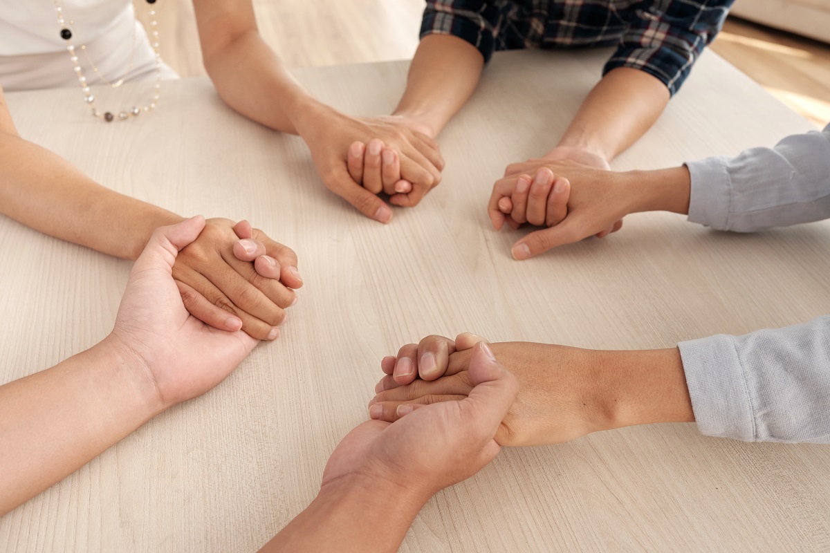 Four unrecognizable people sitting around table holding each other s hands middle small